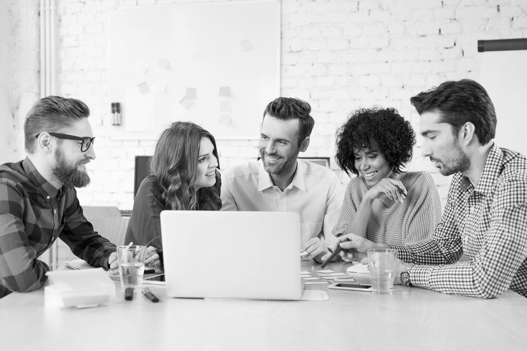 ESS Collaboration Background Hero Faded background of five culturally diverse adults smiling and conversing around a laptop at their workplace