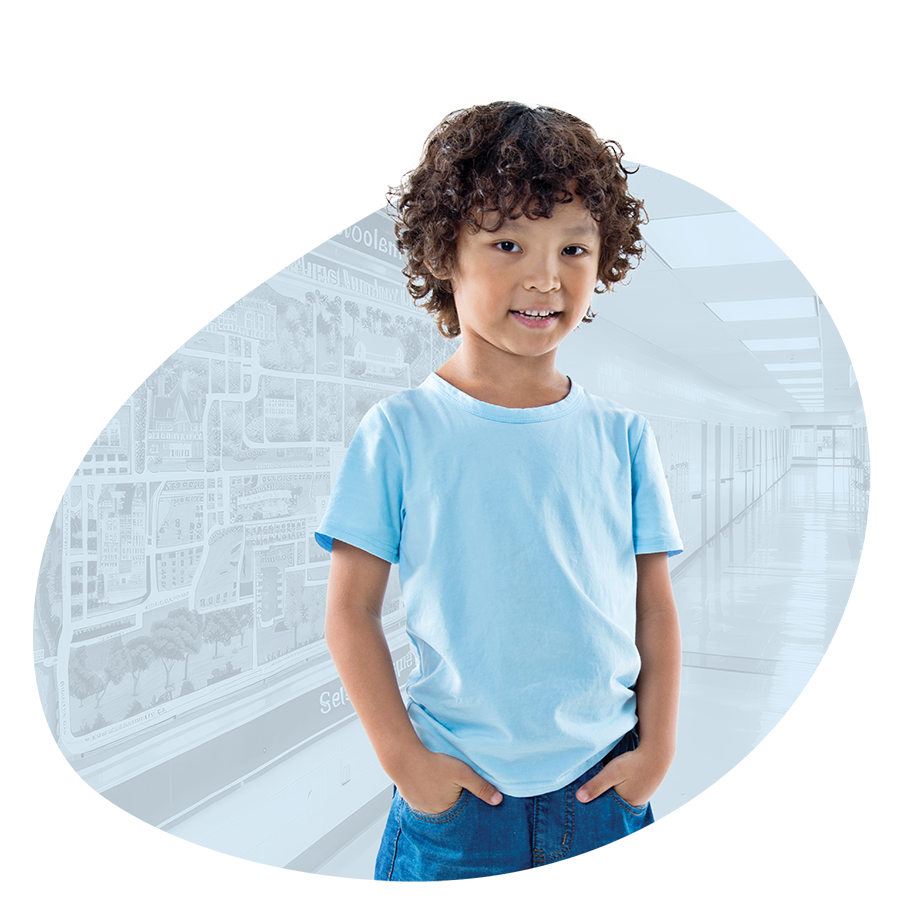 Happy first grade student standing with hands in his pockets in front of a faded background of an elementary school hallway
