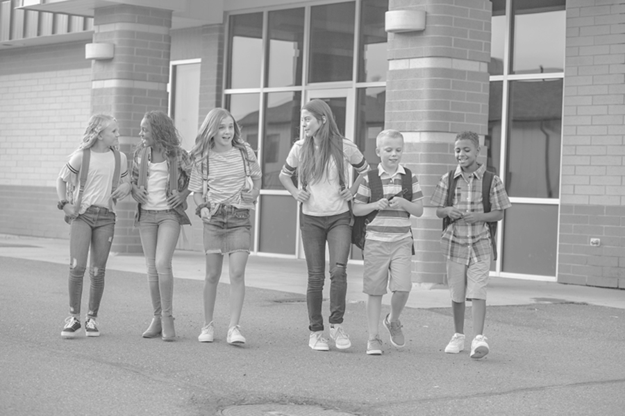 Large, diverse group of kids leaving school at the end of the day. School friends walking together and talking together on their way home after school. Boys and girls